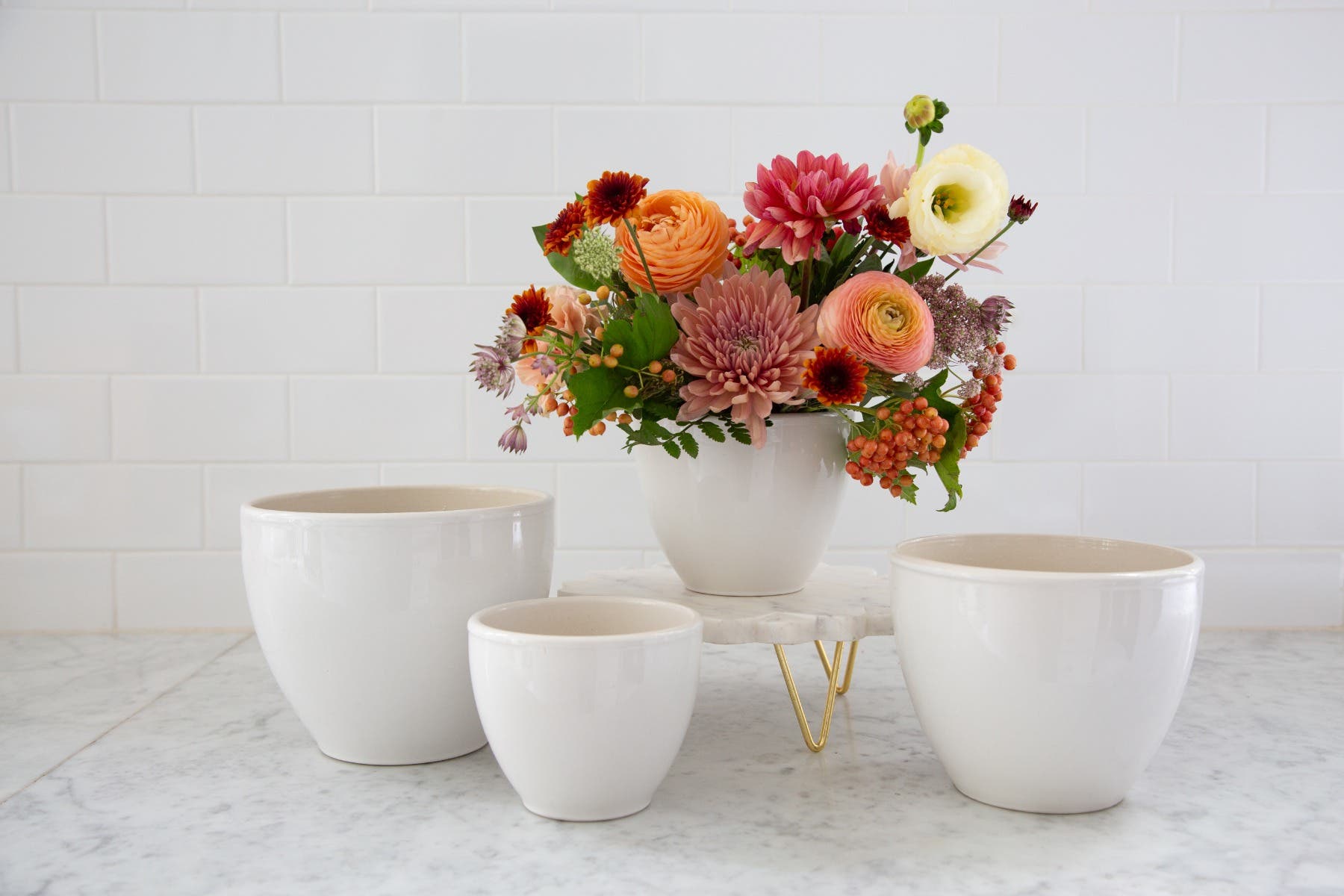 Colorful flowers in a white vase on a marble surface with three white ceramic bowls.