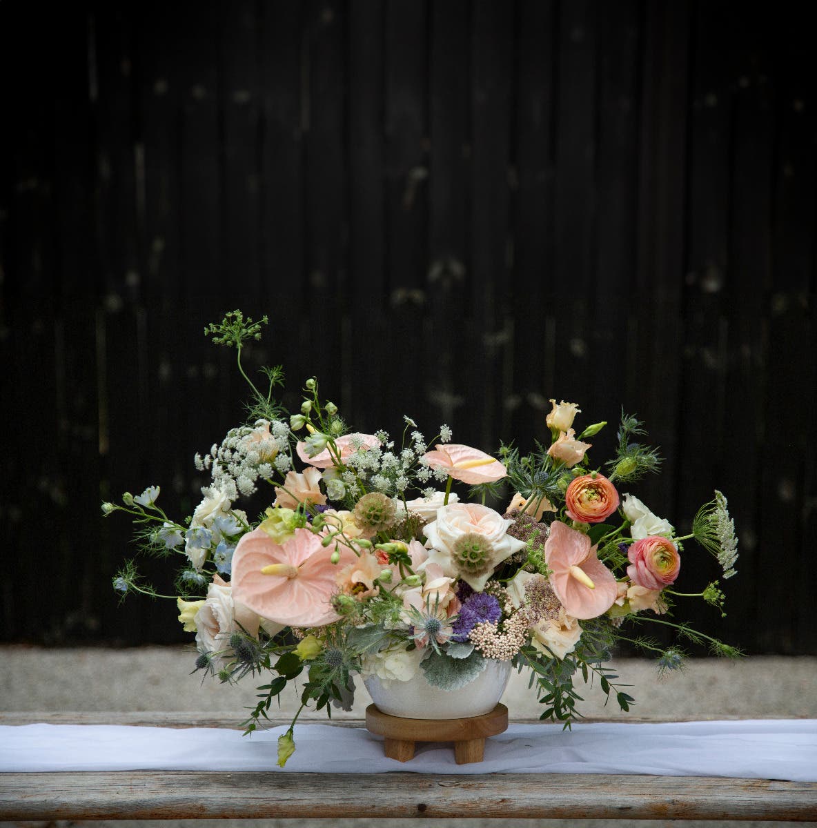 Floral arrangement in a white vase on a wooden surface with a dark background